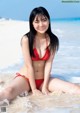 A woman in a red bikini sitting on the beach.