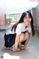 A young woman in a school uniform crouching down on the ground.