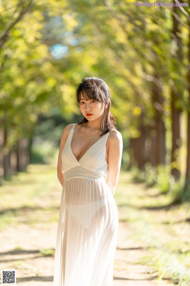 A woman in a white dress standing in a park.