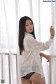 A woman in a white shirt and black panties posing by a window.