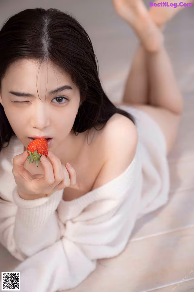 A woman laying on the floor eating a strawberry.