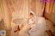 A woman in a wedding dress sitting on a bed.