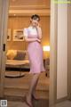 A woman in a pink dress standing in a hotel room.